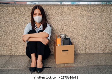 Sad Young Asian Woman With Box Of Items Sitting Alone On Footbridge Flooring After Being Laid Off From Job Due To Covid-19 Pandemic