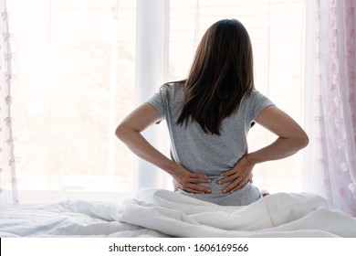 Sad Young Asian Woman Touching Back Feeling Backache Morning Discomfort Low Lumbar Muscular Kidney Pain Sit On Bed After Waking Up Concept Of Woman Stretching Suffering From Sudden Back Pain.