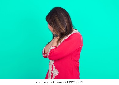 Sad Young Beautiful Moroccan Woman Wearing Traditional Caftan Dress Over Green Background Crying Covering Her Face With Her Hands.