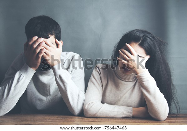 暗い背景にテーブルに座っている悲しい若い夫婦 の写真素材 今すぐ編集