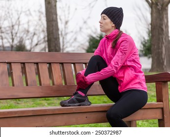 Sad young female athlete sitting on a bench on a cold winter day in the track of an urban park.
