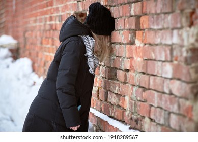 The sad young girl leaned her head against the brick wall