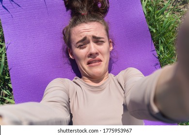 A Sad Young Girl Takes A Selfie On Her Phone. The Athlete Lies On The Yoga Mat Holding The Smartphone In Front Of Her. Conversation Via Video Link At Half-time