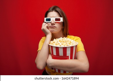 Sad Young Girl Watching A Bad, Boring Movie In 3d Glasses And With Popcorn On A Red Background, Copy Space