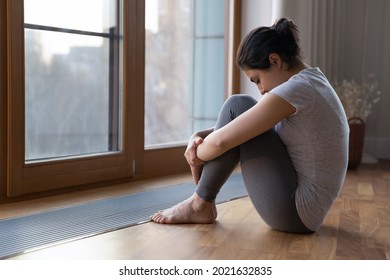 Sad young Indian woman sit look in distance window feel depressed lonely lack communication at lockdown at home. Unhappy upset mixed race female loner outcast suffer with anxiety. Depression concept.