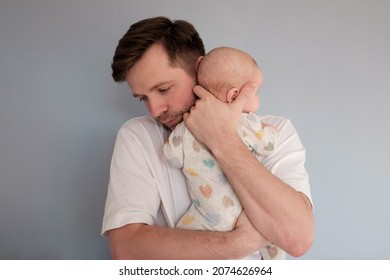 Sad Young Man Holding A 2 Months Old Baby, Isolated On Blue Background