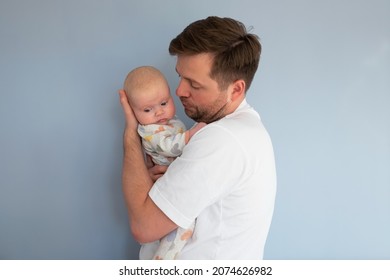 Sad young man holding a 2 months old baby, isolated on blue background