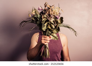 A Sad Young Man Is Holding A Bouquet Of Dead And Withered Flowers