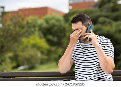 sad young man receives bad news on the phone sitting alone on a park bench - Powered by Shutterstock