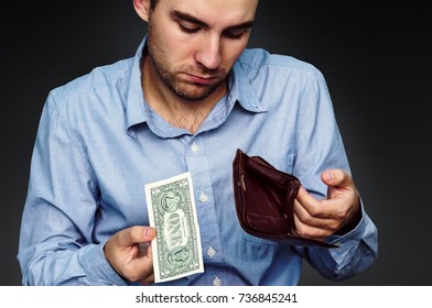a sad young man shows that he has in the wallet a one dollar. Hands close-up holding one dollar and a leather purse. Poverty and unemployment.
