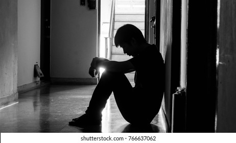 a sad young man sitting in the dark leaning against the wall with his back, The sun is in sorrow.