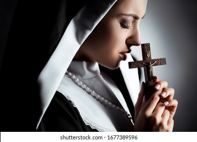 sad young nun praying with cross on grey