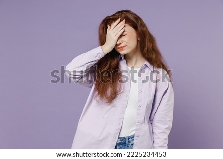 Sad young redhead curly green-eyed woman 20s wears white T-shirt violet jacket put hand on face facepalm epic fail mistaken omg gesture isolated on pastel purple color wall background studio portrait.