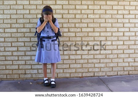 Sad young schoolgirl (female age 9-10) covering her face and crying in school yard. Child bullying concept. Real people. Copy space