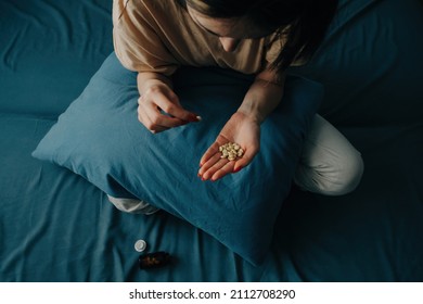 Sad young unrecognizable woman takes antidepressants. A young woman sits on a bed with pills in her hands. - Shutterstock ID 2112708290