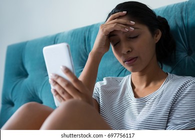 Sad Young Woman Holding Mobile Phone In Bedroom At Home