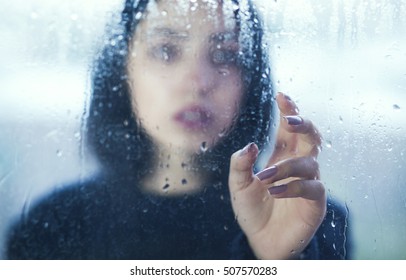 Sad Young Woman Looking Through  Window With A Rain Drops.