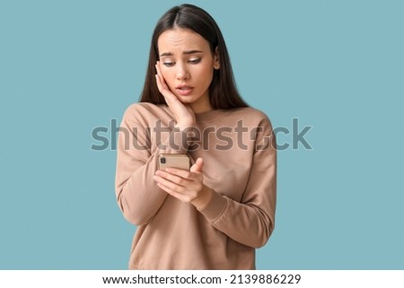 Sad young woman with mobile phone on blue background