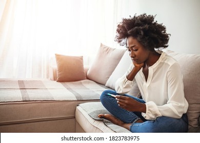 Sad Young Woman With Pregnancy Test At Home. Disappointed african-american girl getting unexpected result from pregnancy test. Woman desperate after reading pregnancy test result