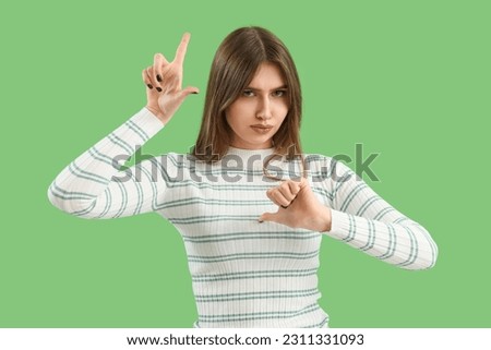 Sad young woman showing loser gesture on green background