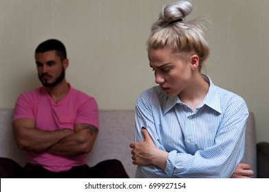 Sad Young Woman Sitting And Looking Away While Man Sitting Separately On Sofa. Young Couple Angry At Each Other. Focus On Female