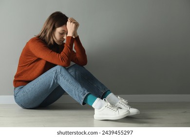 Sad young woman sitting on floor near grey wall indoors, space for text - Powered by Shutterstock