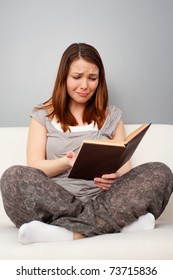 sad young woman sitting on sofa and reading book