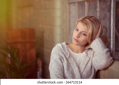 Sad young woman sitting thinking resting her head on her hand on the back of the sofa as she stares at the ground with a serious expression - Powered by Shutterstock