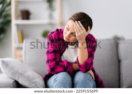 Sad young woman suffering depression hand on head sitting on couch. Anxiety and mental health concept