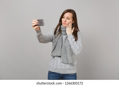 Sad Young Woman In Sweater, Scarf Putting Hand On Cheek, Doing Selfie Shot On Mobile Phone Making Video Call Isolated On Grey Background. Healthy Fashion Lifestyle People Emotions Cold Season Concept