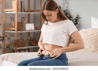 Sad young woman in tight jeans sitting on bed at home. Weight gain concept - Powered by Shutterstock