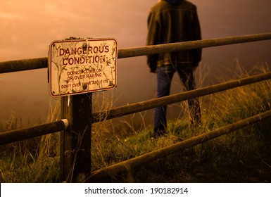 Sad/depressed Man Standing On Edge Of Cliff Behind A Danger Sign