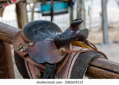 Saddle brown on fence in shallow depth of field. Sport leather saddle, harness for horses on daylight. Western horse saddles on a rack,  ready for dressage training. Equestrian sport background. 