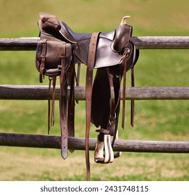 Saddle, horse and farm on ranch fence, riding and equestrian sports in country side. Western, cowboys and field in Texas, stirrup and leather seat or equipment for outdoors exercise in paddock - Powered by Shutterstock