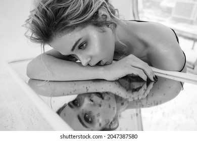 Traurige Attraktive Girl Lay auf Mirror-Tisch und Blick auf Reflection Nahaufnahme Monochrome Fotografie. Eine gedankenvolle europäische Frau mit Visage lädt zum Entspannen auf dem Glastisch ein. Tired Lady im Zimmer