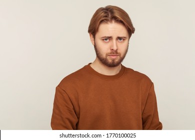 Sadness and resentment emotions. Portrait of unhappy bearded man in sweatshirt looking at camera with upset vexed face, depression from life problem. indoor studio shot isolated on gray background