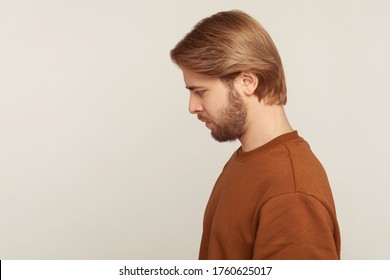 Sadness and resentment emotions. Profile of unhappy bearded man in sweatshirt looking down, bowing head with upset vexed face, depression from life problem. studio shot isolated on gray background