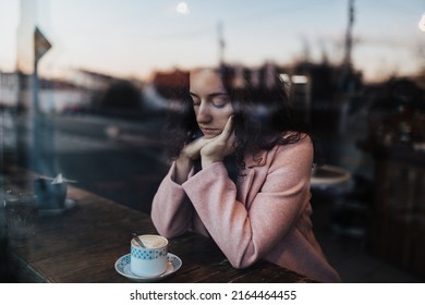 Sad,pensive Young Woman Drinking Coffee And Looking Out Of The Cafe Window.