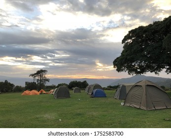 Safari campsite with tents in safe distance to each other on green grass on the edge of Ngorongoro crater in Tanzania at cloudy sunset