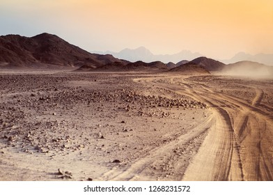 Safari and travel to Africa - extreme adventures or science expedition in a stone desert. Sahara desert at sunrise - mountain landscape with dust on skyline, hills and traces of the off-road car.