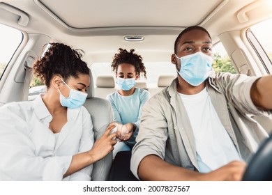 Safe Car Travel During Pandemic. Black Family Wearing Face Masks And Using Hands Sanitizer Spray Riding Auto. Coronavirus Protection In Summer Road Trip During Covid-19 Pandemic Concept