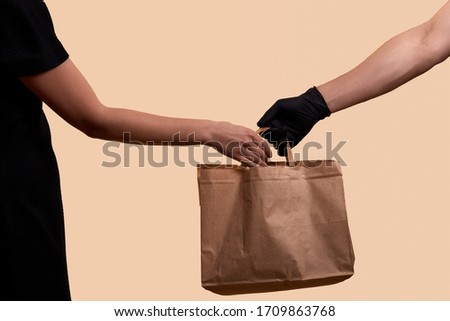 safe delivery for quarantine male hand in black latex glove gives paper bag to woman in black dress