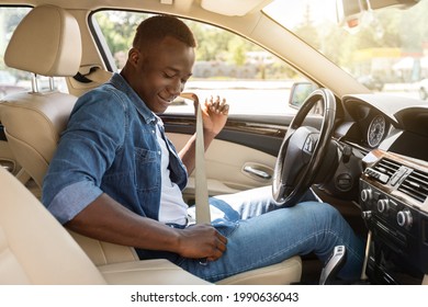 Safe Driving Concept. Positive Young Black Man Fastening Car Seat Belt, Side View, Copy Space. Cheerful African American Guy Beginning Car Trip, Renting Nice Cozy Auto For Travelling