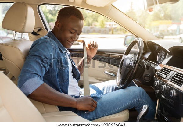Safe driving\
concept. Positive young black man fastening car seat belt, side\
view, copy space. Cheerful african american guy beginning car trip,\
renting nice cozy auto for\
travelling