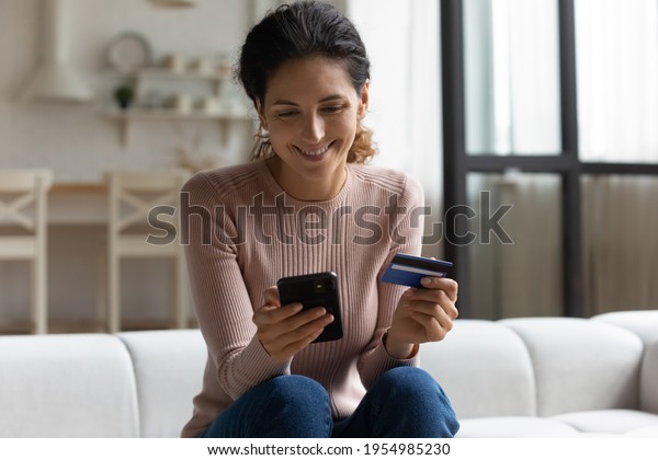 Safe mobile banking. Smiling latina lady client hold\
mobile phone credit bank card do online shopping provide internet\
payment. Happy young woman enjoy easy fast secure transferring\
money in ebank app