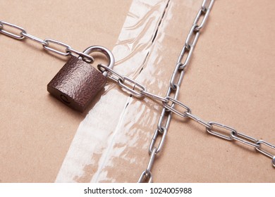 Safe Reliable Delivery Of Cargo In Safety Without Theft. The Cardboard Box Is Wrapped In A Chain With A Closed Lock