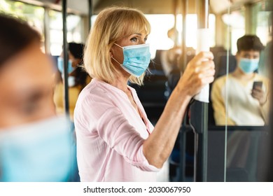 Safe Ride. Portrait of serious senior woman wearing protective face mask taking crowded bus holding handle, standing inside and looking out of window. Rush hour traffic, new normal life rules, covid