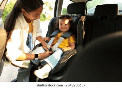 Safe Travels Together. Chinese Mom Ensuring Child's Safety, Securing Toddler Daughter in Car Seat for a Smooth and Secure Automobile Ride, Adjusting Harness Straps In Baby Chair in Auto - Powered by Shutterstock