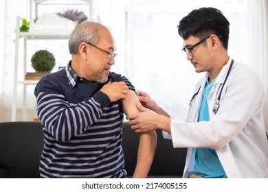 Safe Vaccination For Old People. Elder Man In Medical  Getting Flu Or Covid-19 Vaccine Sitting On Sofa At Home. Asian Doctor Or Nurse Giving Flu Or Covid-19 Shot To Senior.