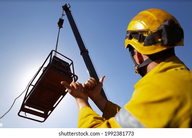 Safe work practice rigger wearing fall protection helmets giving crane operator hand signal by holding up two hand against each other pointing boths thump out meant crane boom is giging out slowly    